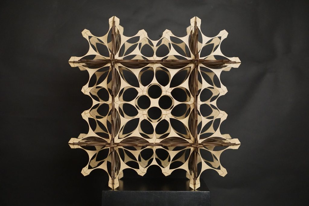 Front view of a pale modular model with repeated curved openings against a dark background.